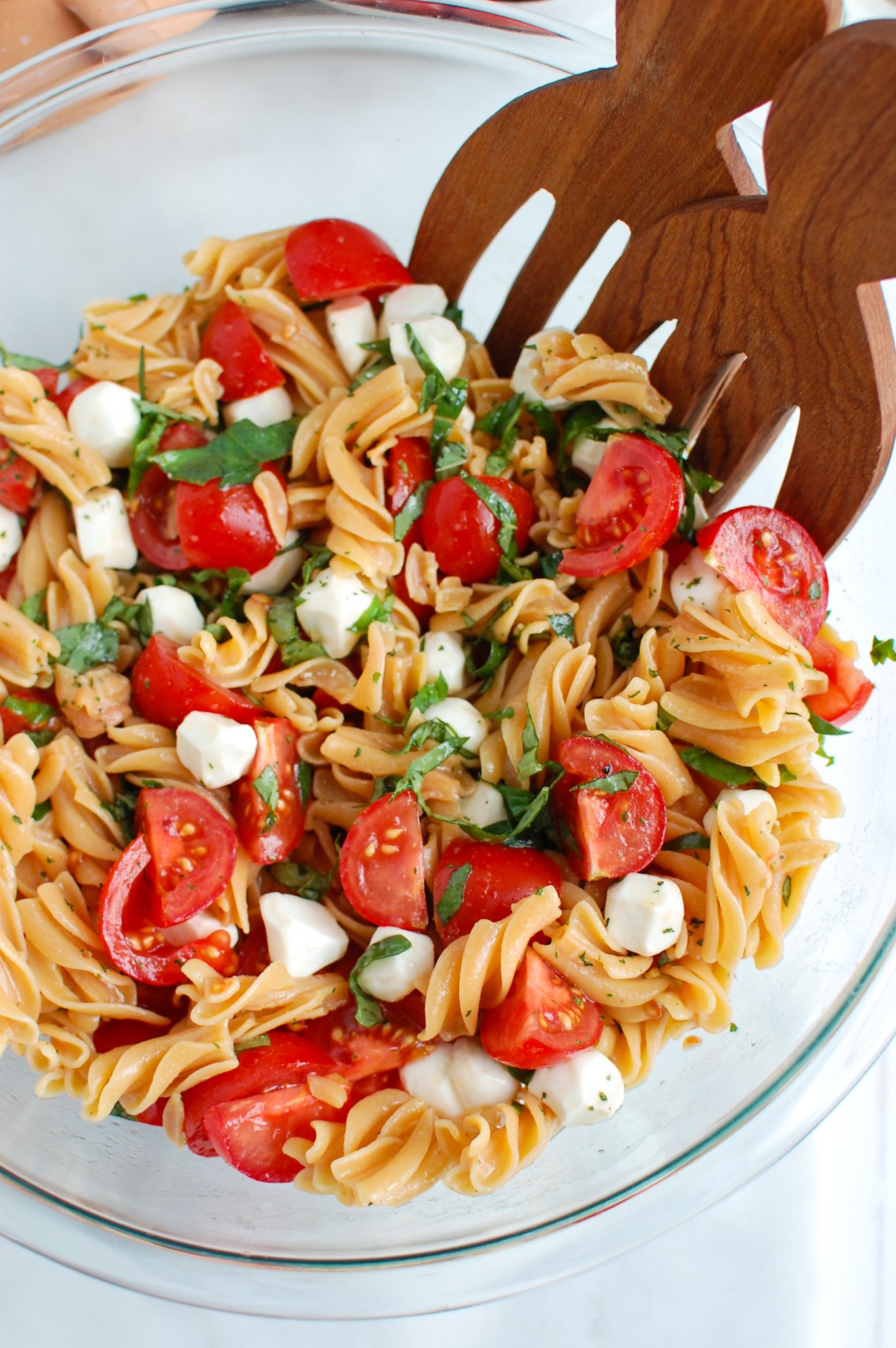 Caprese Pasta with wooden tongs.