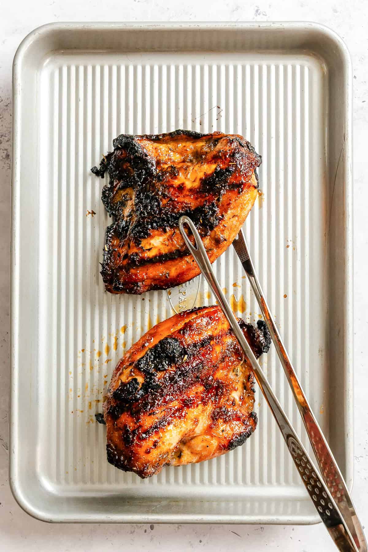 Grilled Honey Lime Chicken on a baking sheet with tongs