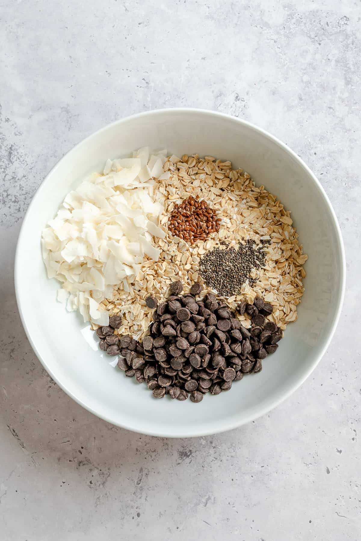 Mixing oats, coconut flakes, and chocolate chips in a large bowl for no-bake oatmeal bites