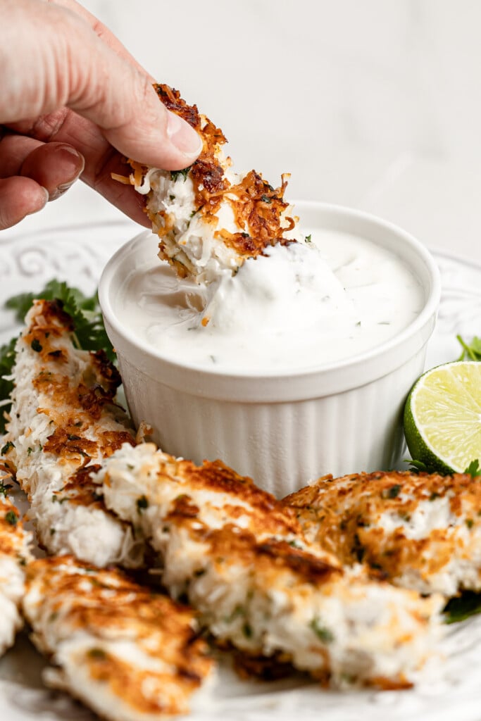Coconut Chicken Tenders being dipped into aioli