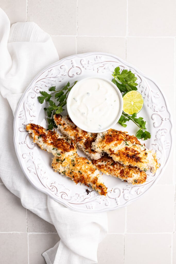 Coconut Chicken Tenders on white plate with dipping sauce 