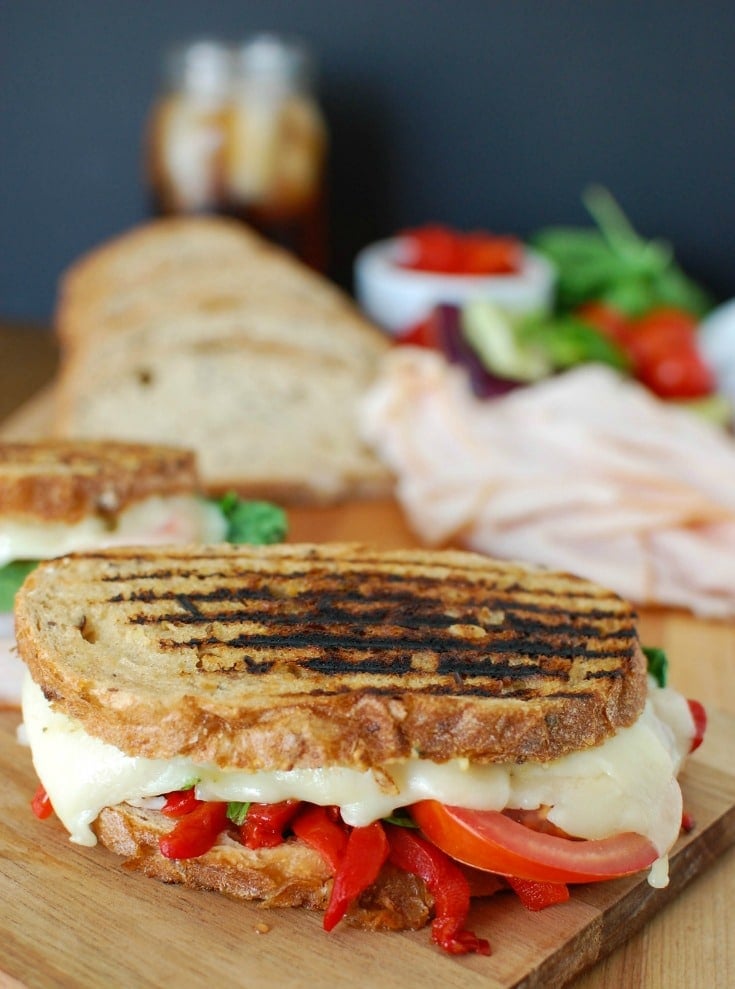 Mediterranean Turkey Hummus Panini makes a great lunch packing your favorite Mediterranean flavors into a warm, flavorful sandwich. Garlic and Herb hummus is spread on your favorite bread and topped with smoked turkey, roasted red peppers, spinach, sliced tomatoes, artichokes and havarti cheese to create the ultimate sandwich.