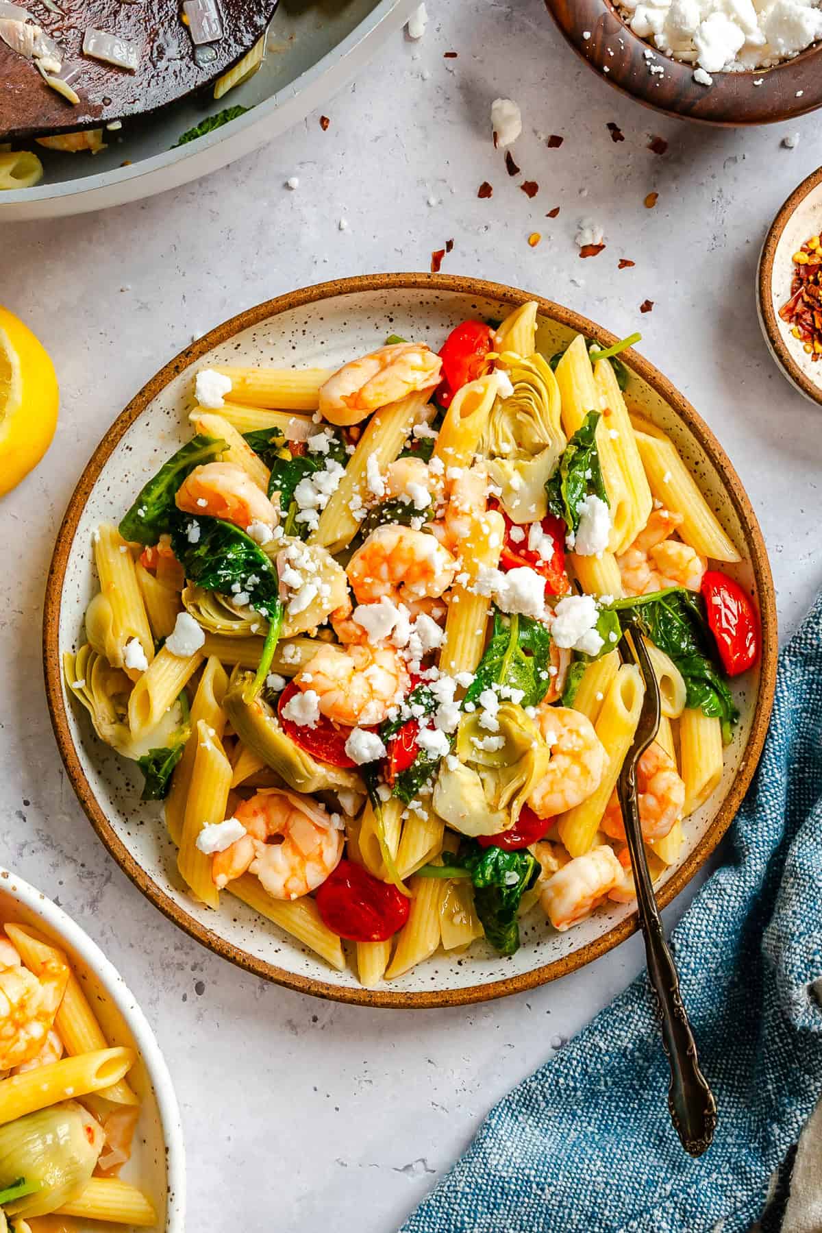 Close up of penne pasta tossed with pink shrimp, wilted baby kale, and artichoke hearts