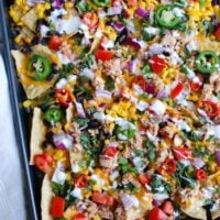 Southwestern Salmon Nachos take traditional nachos to a new level mixing salsa and salmon together and topping that with black beans, corn, shredded cheese, tomatoes, red onion, cilantro, green onion, jalapeños, red chiles and a drizzle of sour cream. These nachos are backed to perfection and are a nice lunch for Father's Day or football season.
