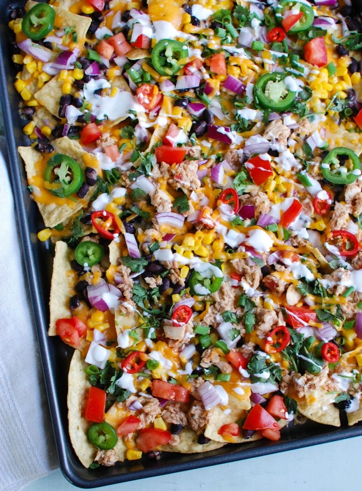 Southwestern Salmon Nachos take traditional nachos to a new level mixing salsa and salmon together and topping that with black beans, corn, shredded cheese, tomatoes, red onion, cilantro, green onion, jalapeños, red chiles and a drizzle of sour cream. These nachos are baked to perfection and are a nice lunch for Father's Day or football season. 