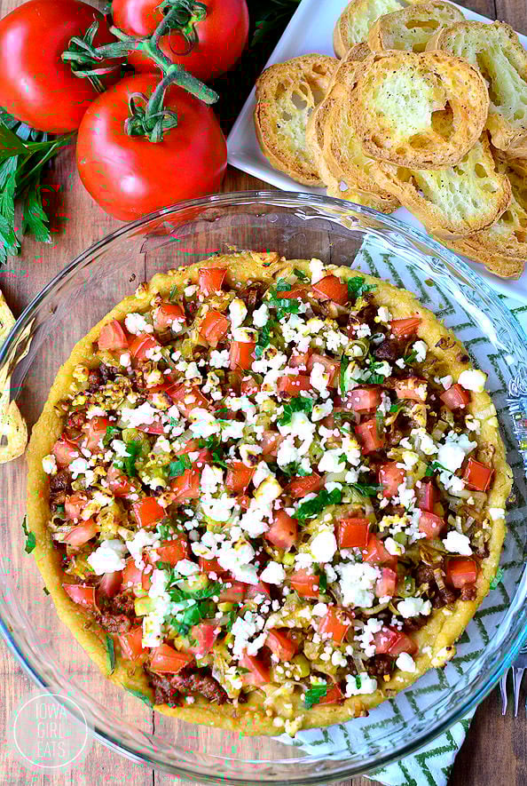 Store-bought hummus is spread into a pie pan then topped with browned sausage, sauteed leeks, chopped tomatoes, and crumbled feta cheese with crostini made from baguettes
