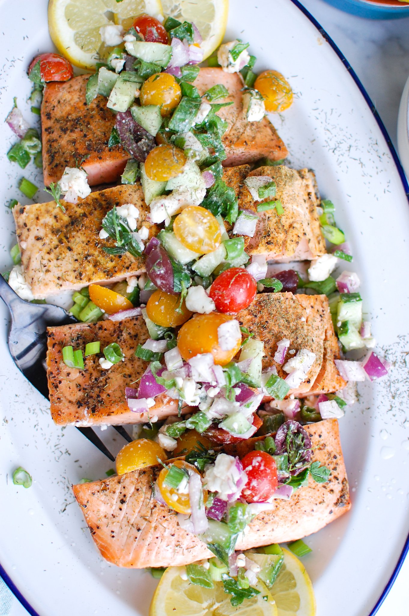 Mediterranean Salmon on white platter topped with fresh tomatoes, feta cheese, and herbs. 