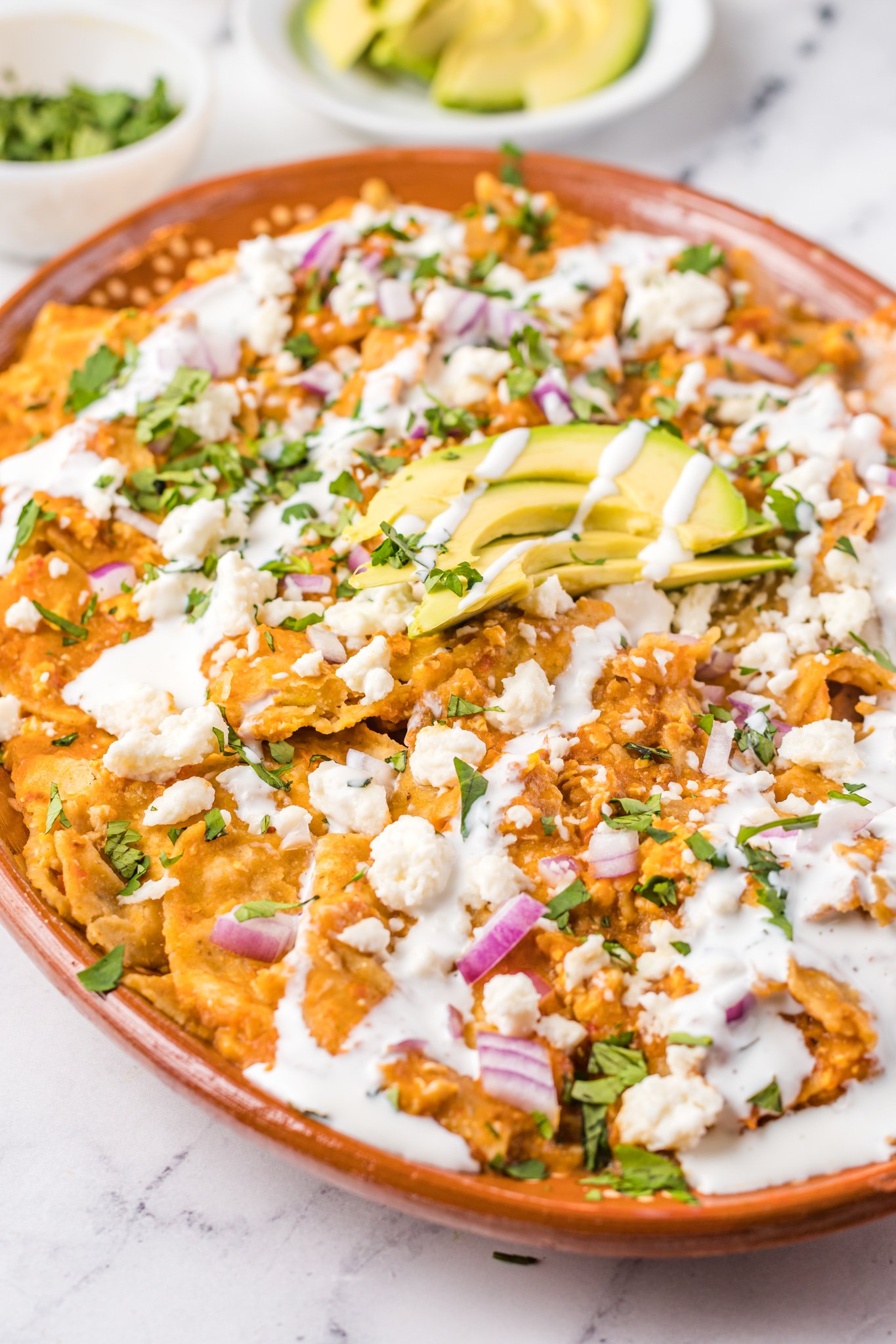 Chilaquiles Rojos Recipe on a platter with avocado on top.