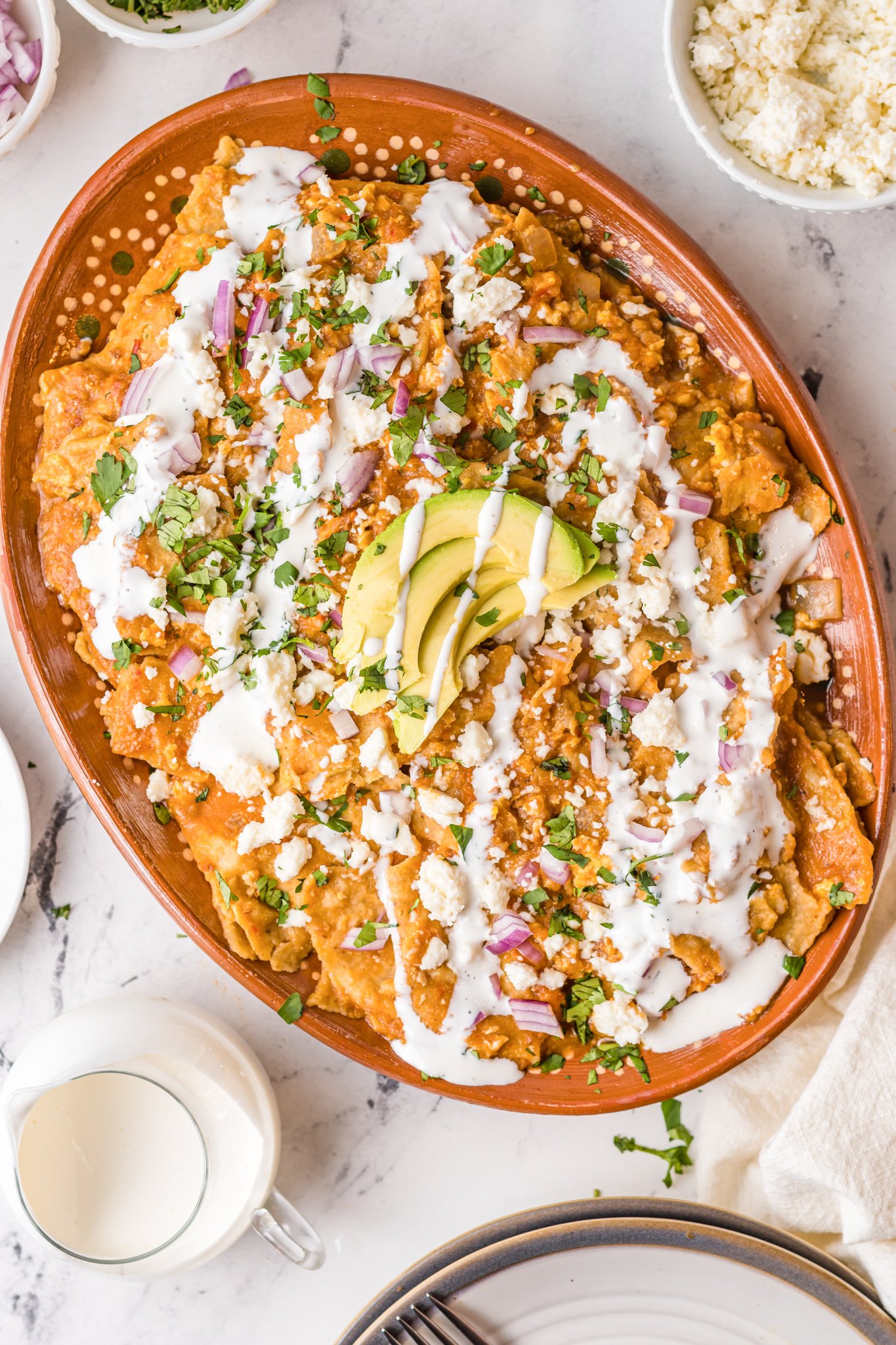Chilaquiles Rojos Recipe in a large platter topped with avocado slices and mexican crema 