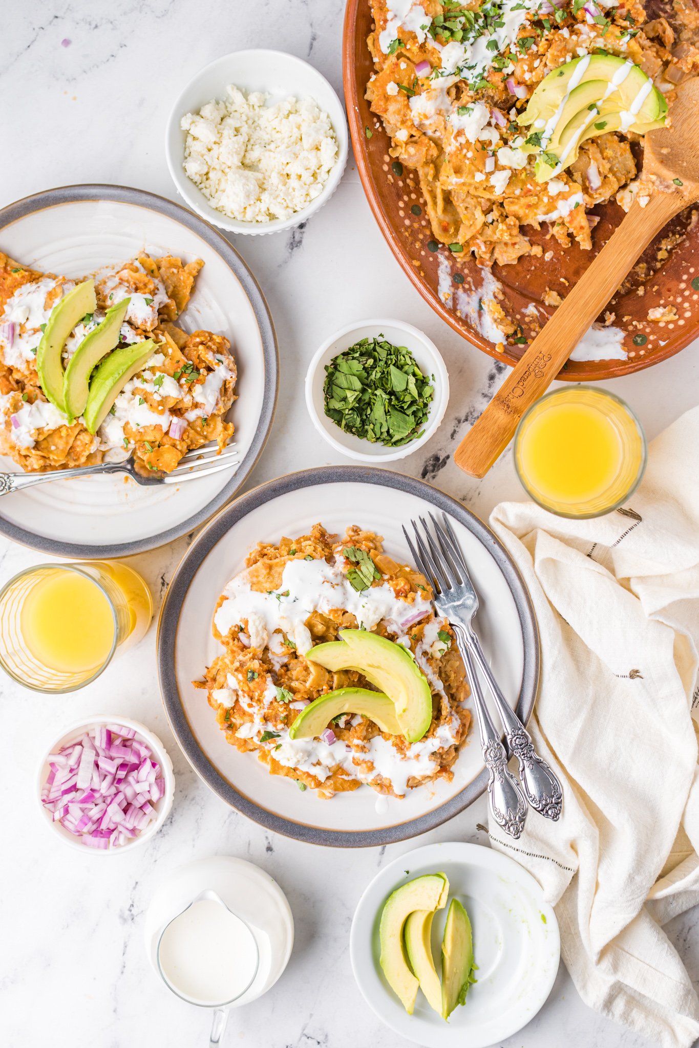 a plate of mexican food with avocado on top, and orange juice in a glass