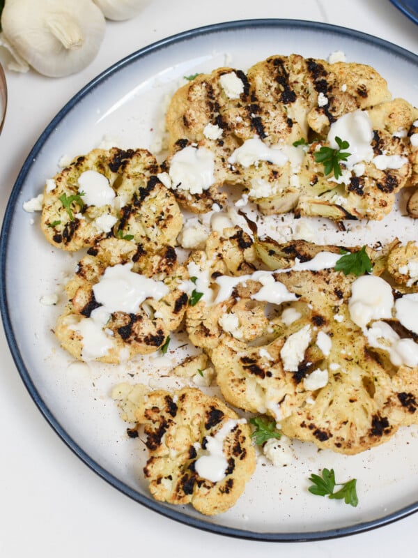 Grilled Cauliflower Steaks with Yogurt Tahini Sauce on a white plate.