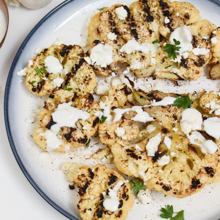 Grilled Cauliflower Steaks with Yogurt Tahini Sauce on a white plate.