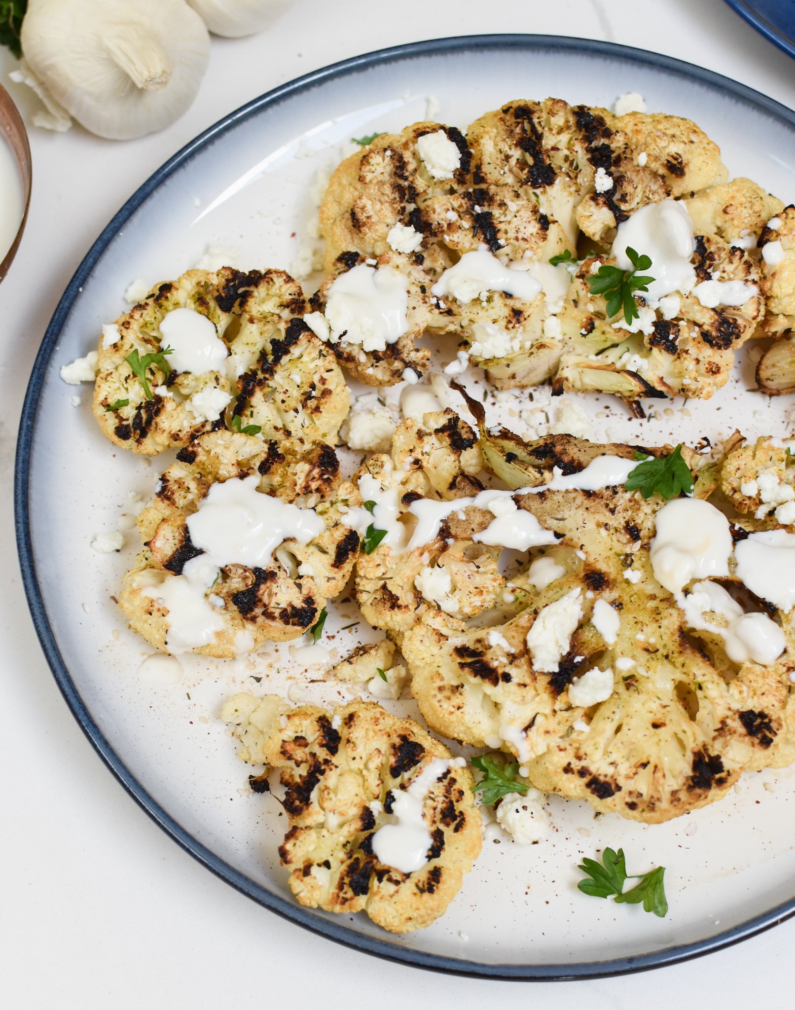 Grilled Cauliflower Steaks with Yogurt Tahini Sauce on a white plate.