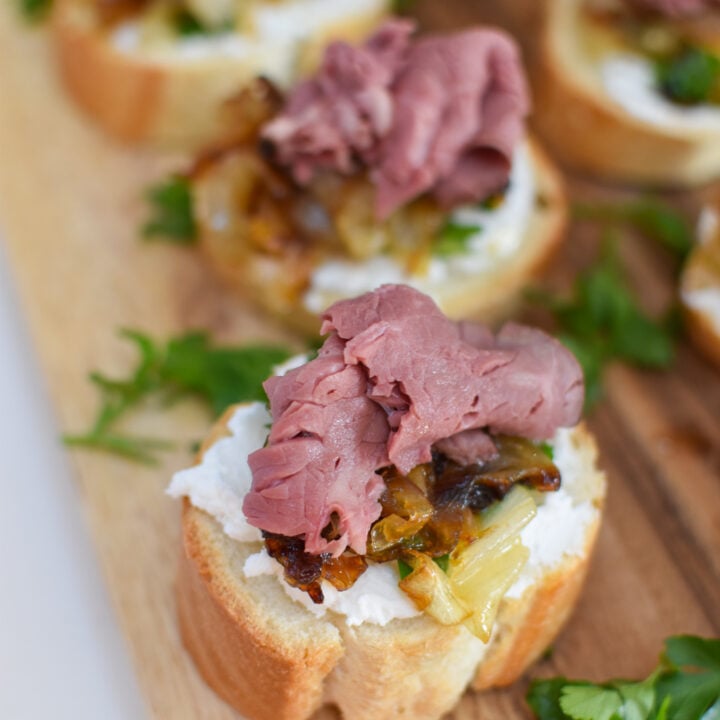 Beef Crostini with Caramelized Onion and Goat Cheese on a cutting board.