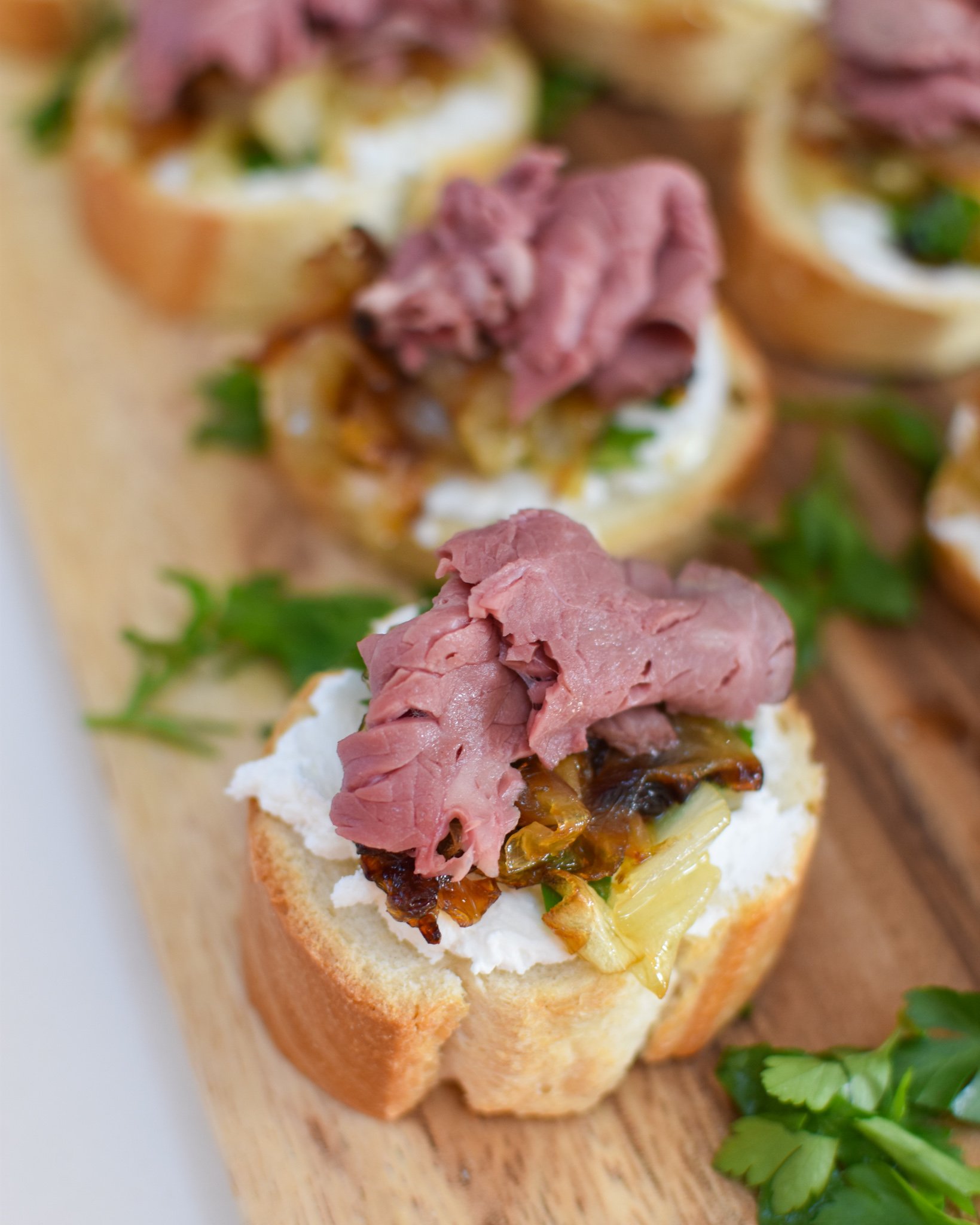 Beef Crostini with Caramelized Onion and Goat Cheese on a cutting board. 