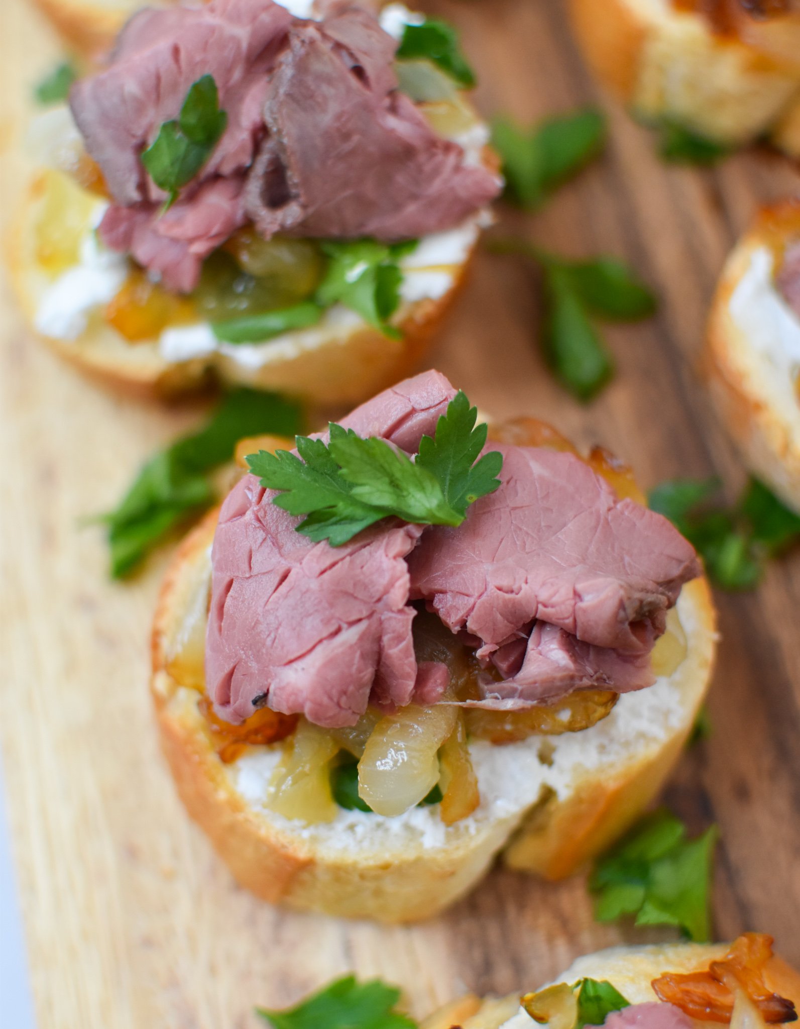 Beef Crostini with Caramelized Onion and Goat Cheese on a cutting board.