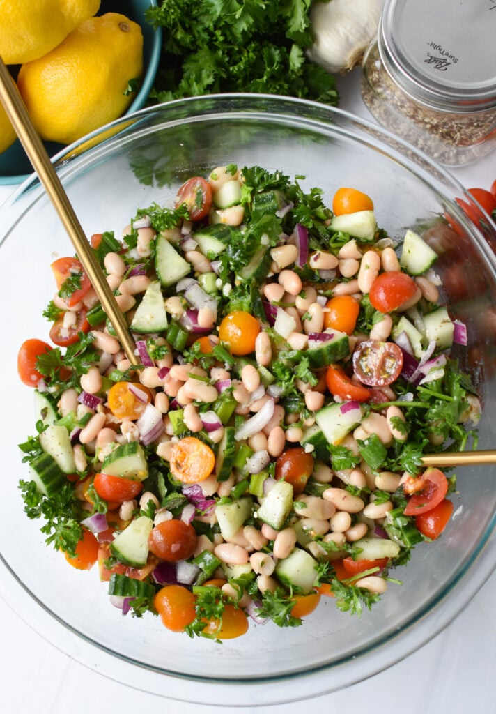 Mediterranean White Bean Salad with gold serving spoons.