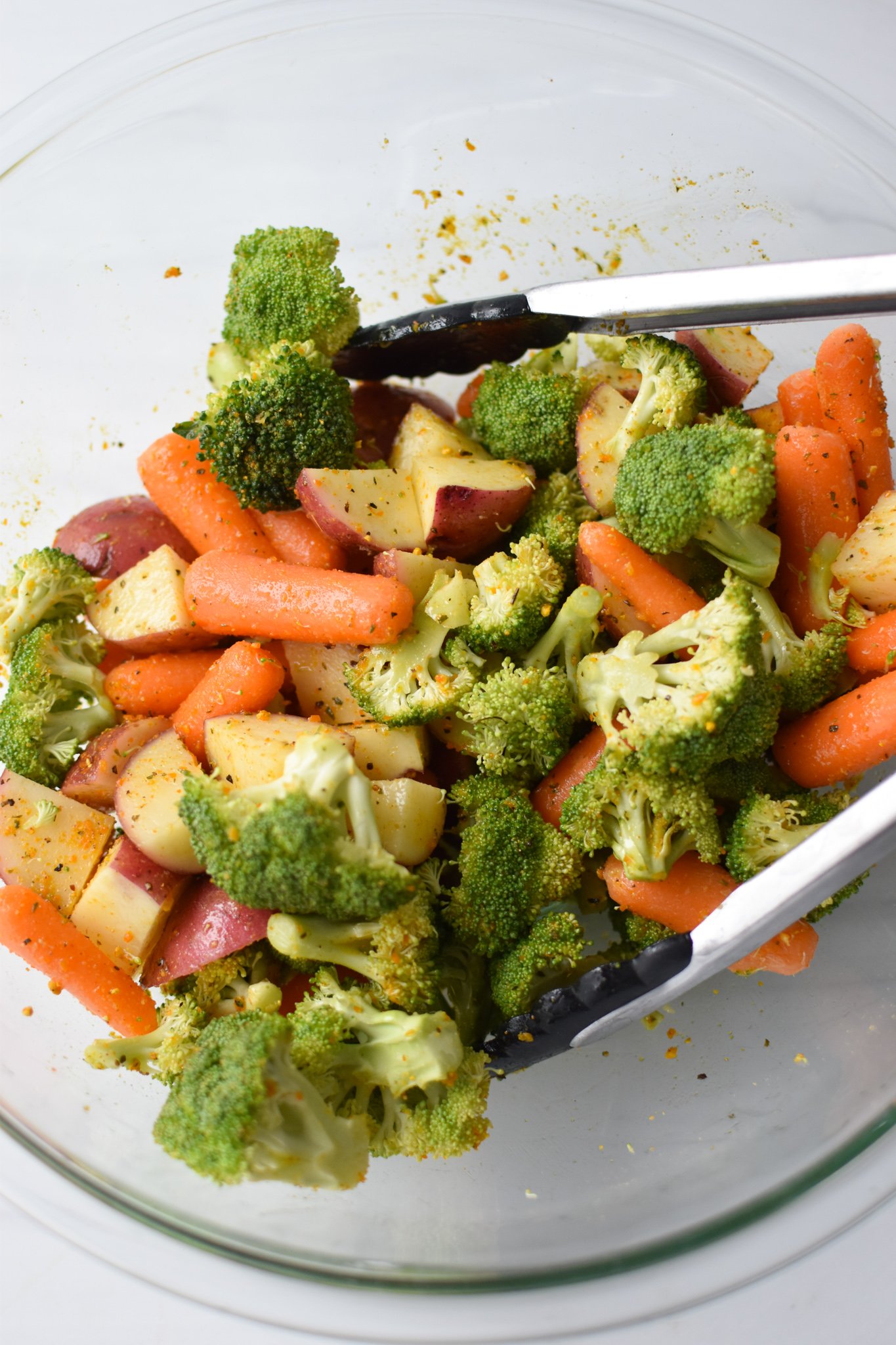 Sheet Pan Lemon Parmesan Chicken Tenders vegetables and potatoes with spices in a bowl. 