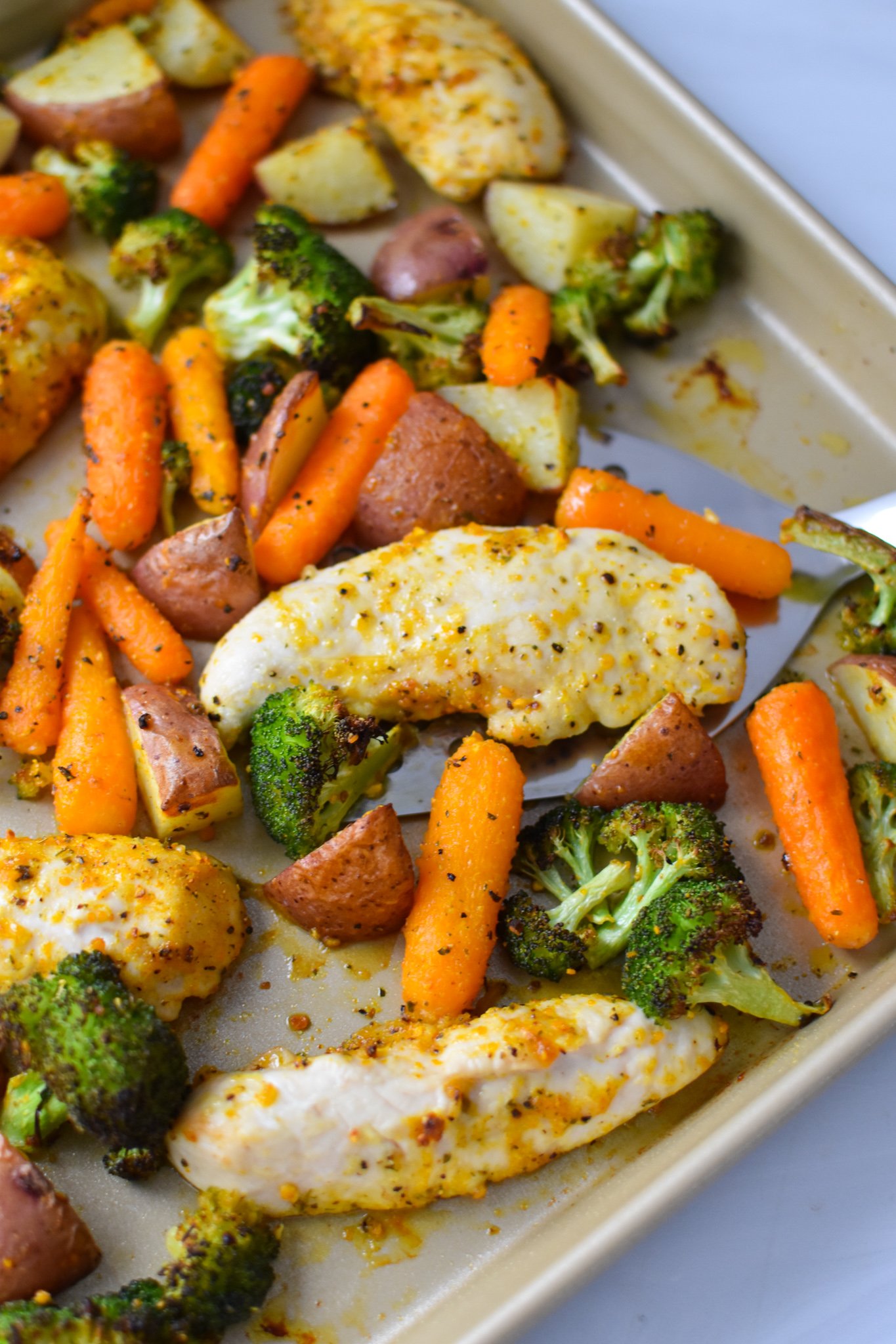 Sheet Pan Lemon Parmesan Chicken Tenders with a spatula on a baking sheet. 