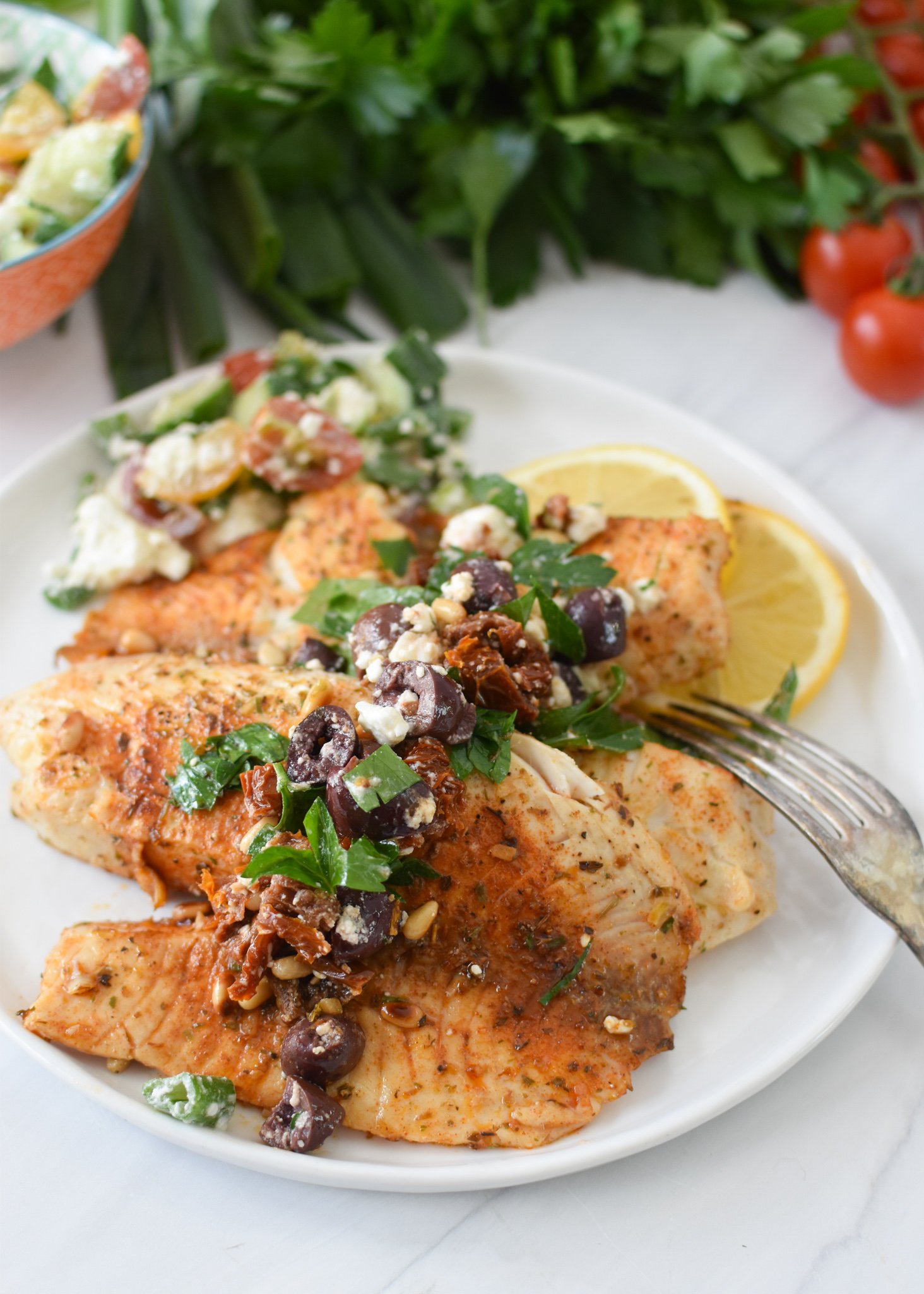 Greek Baked Tilapia with a fork on a white plate.