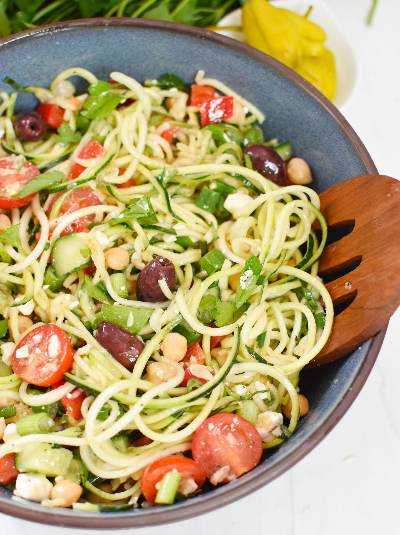 Mediterranean Zucchini Pasta Salad in a blue bowl with wooden tongs. 