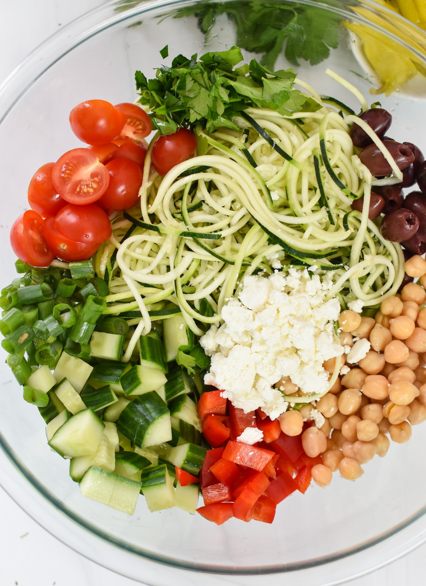 Mediterranean Zucchini Pasta Salad ingredients in a glass bowl. 