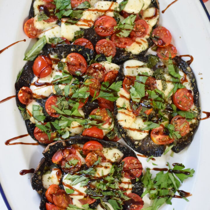 Caprese Stuffed Portobello Mushrooms with balsamic drizzle on a white platter.