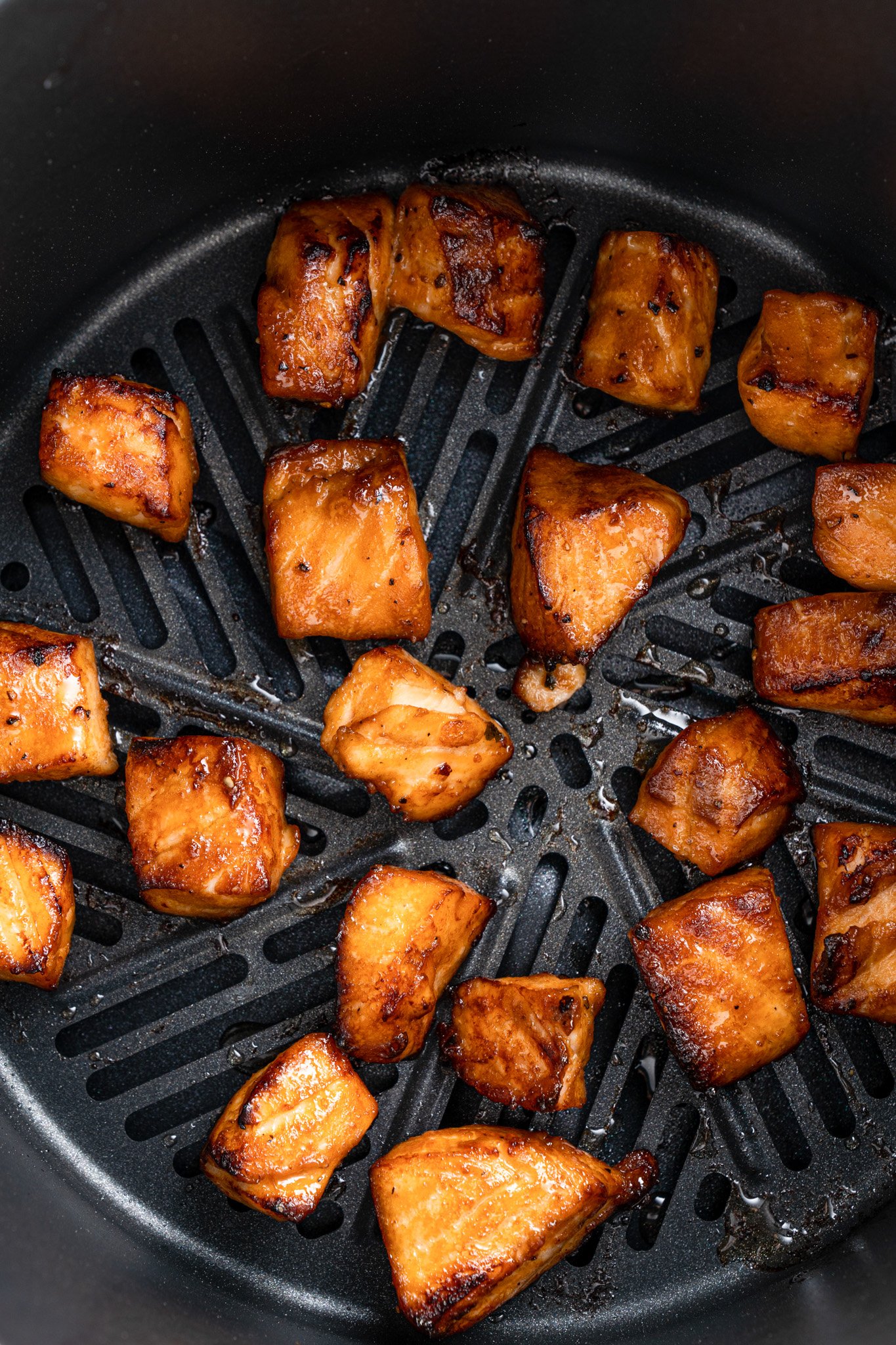 Chunks of glazed salmon are evenly spaced and cooked inside an air fryer basket. The pieces are golden brown with a slight char, indicating they are cooked and ready to eat.