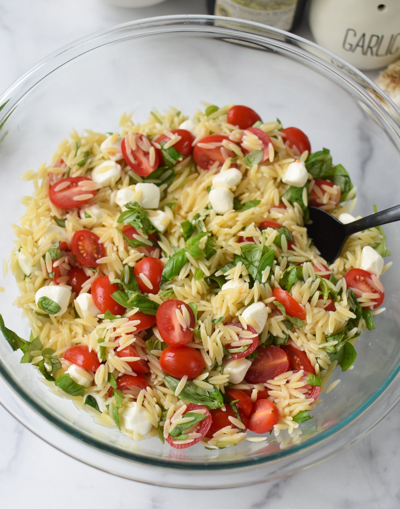 Caprese Orzo Pasta Salad with dressing in glass bowl. 