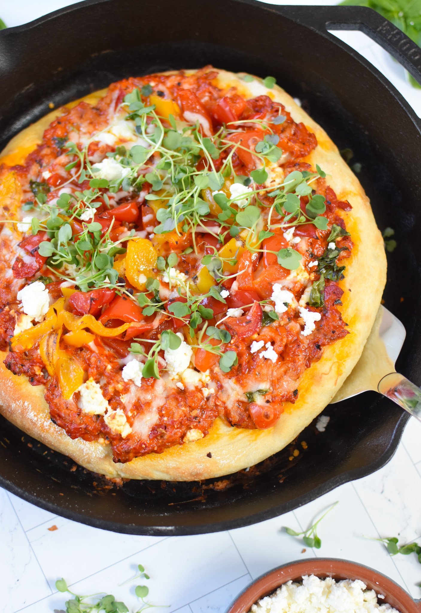 Cast Iron Mediterranean Pizza in a skillet with a spatula. 