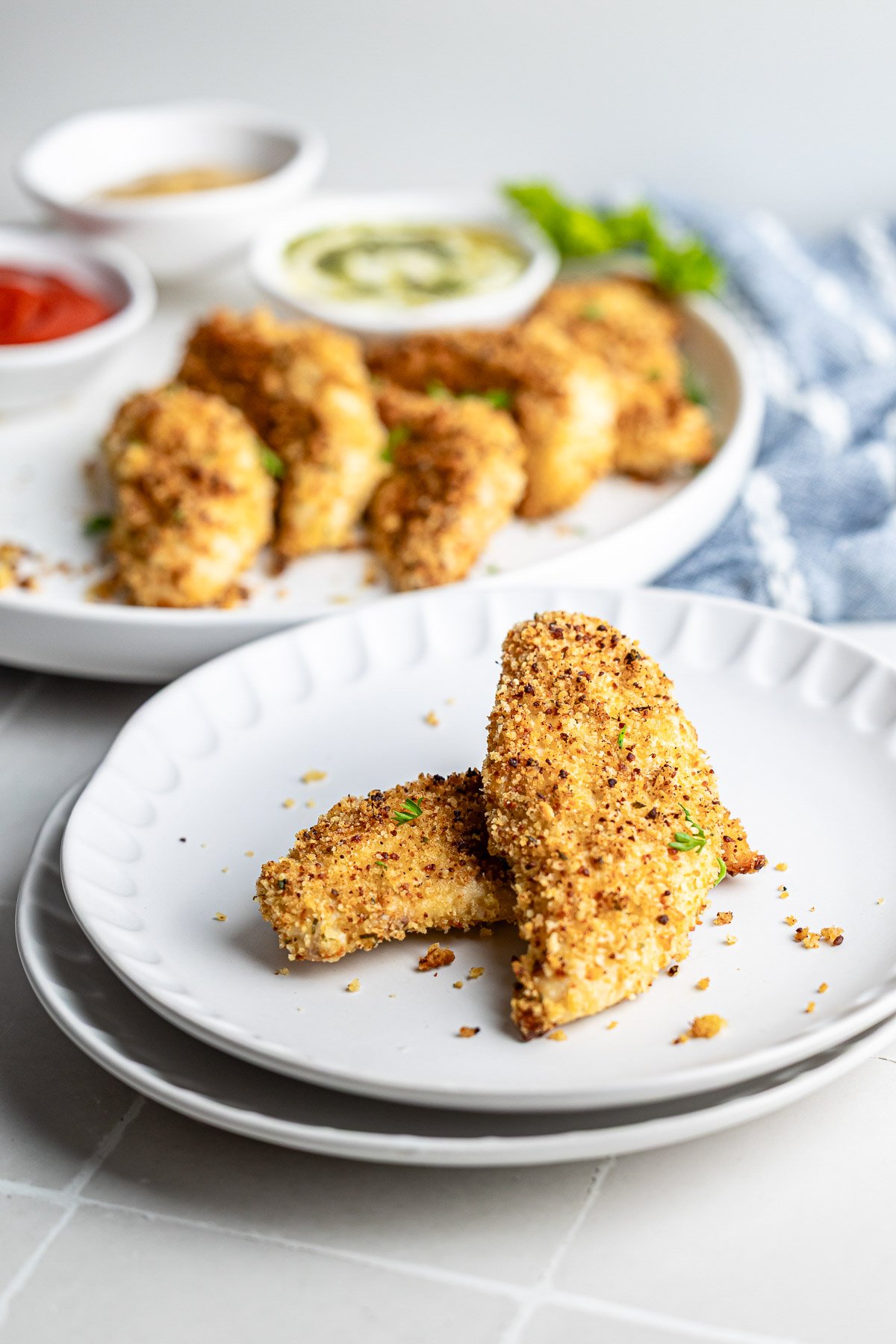 Baked chicken tenders plated on a white dish with herbs for garnish.