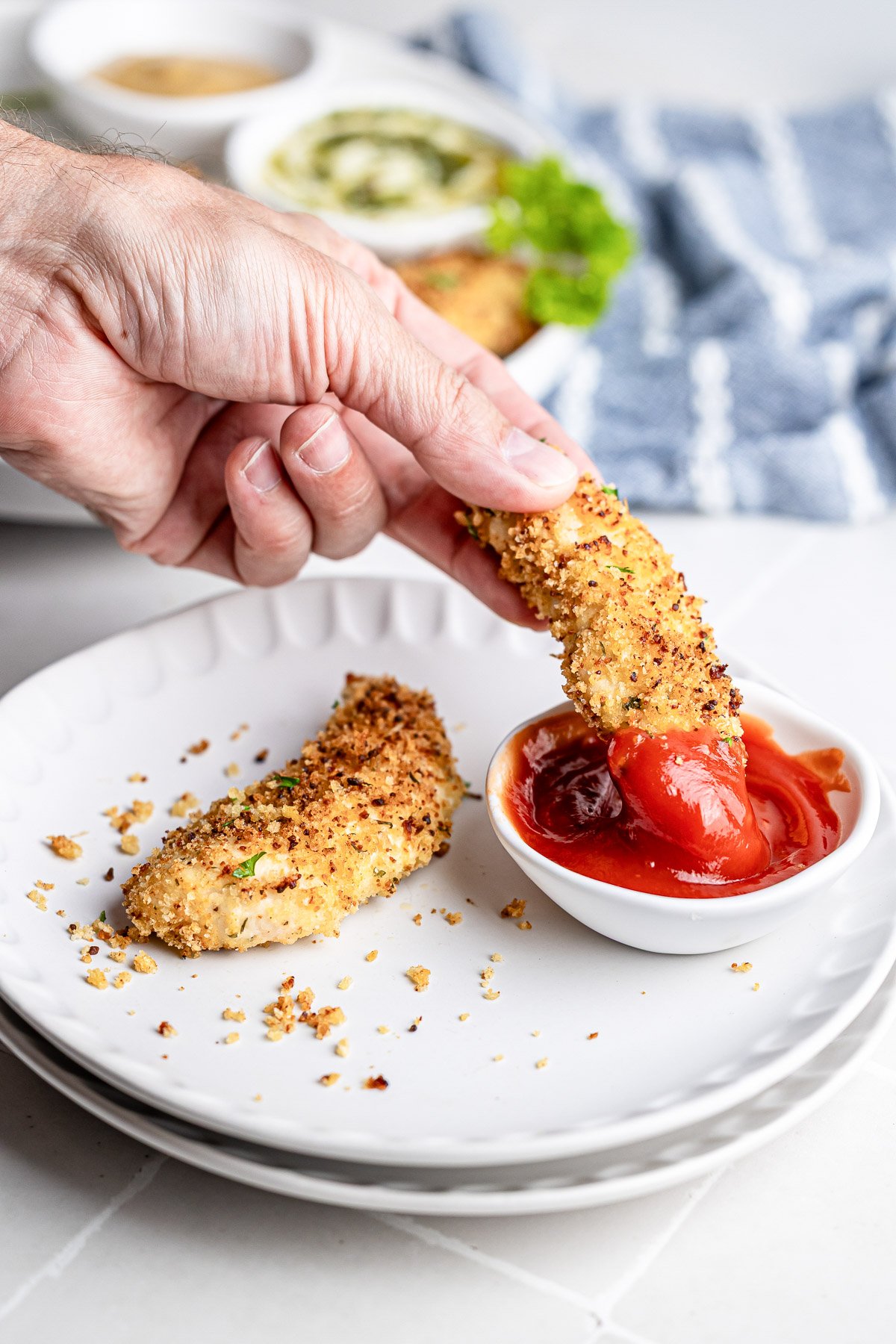 Baked chicken tender being dipped into a small bowl of ketchup.