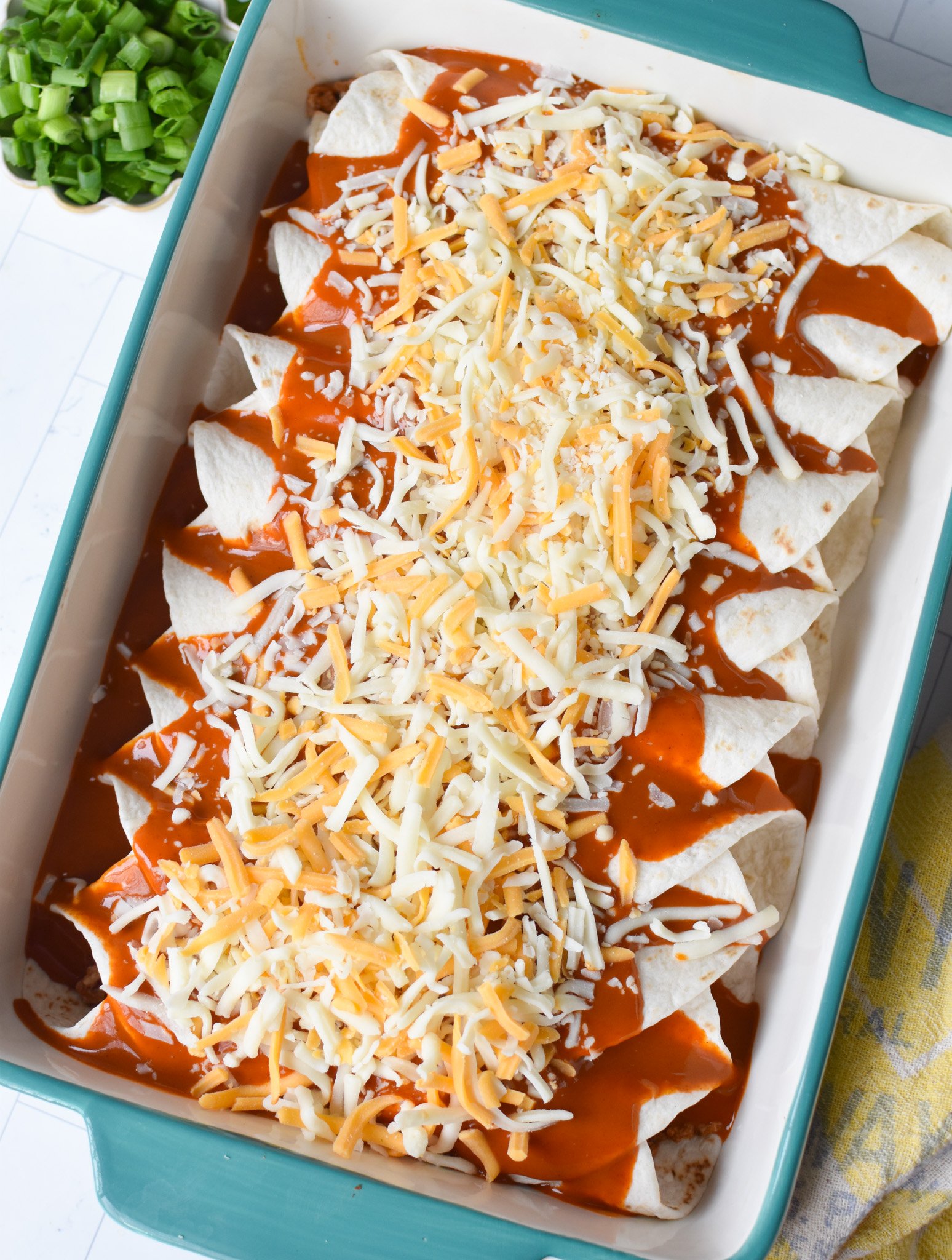 enchilada sauce and cheese on top of rolled tortillas