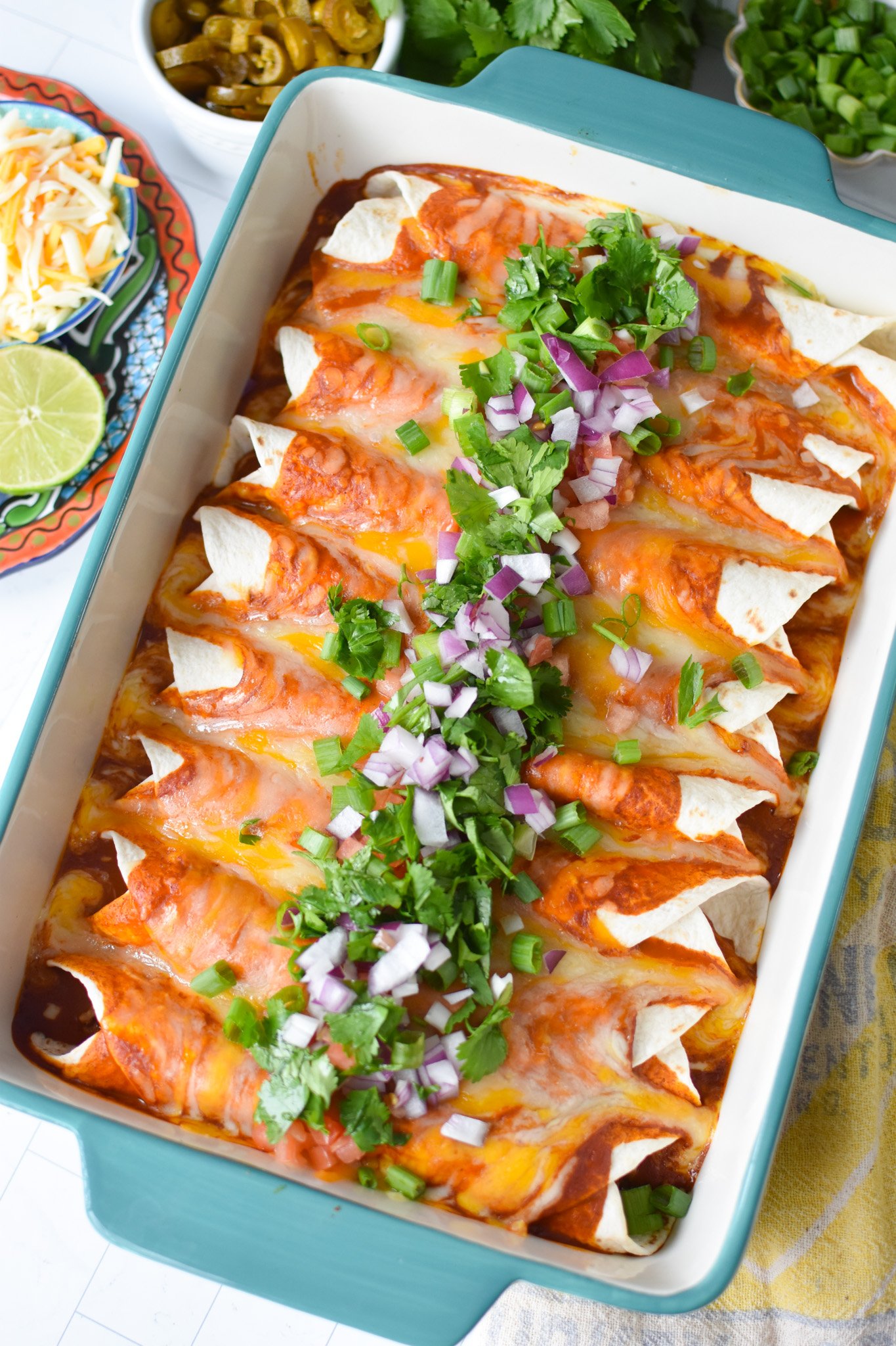 a casserole dish filled with enchiladas and fresh toppings 