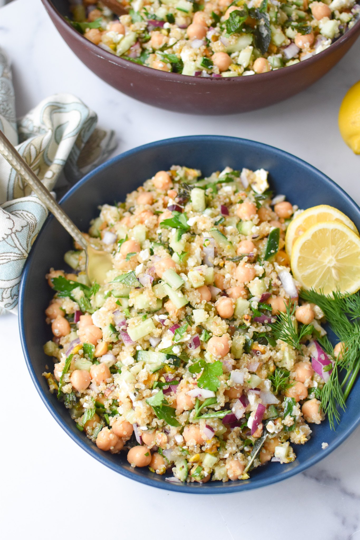a Jennifer aniston salad in a blue mixing bowl with lemon wheels and fresh dill. 