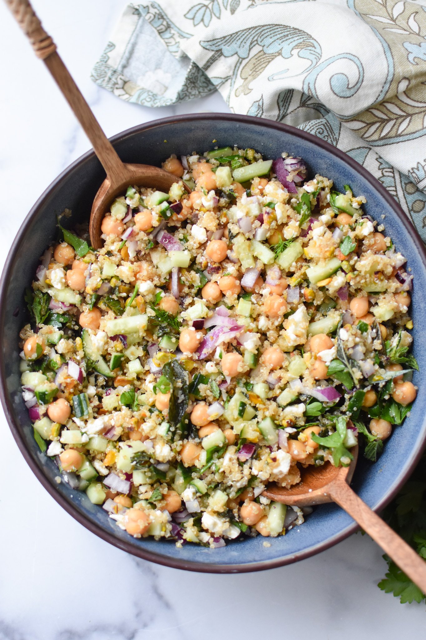 an overhead shot of a Jennifer Aniston salad in a blue salad bowls with wooden spoons on each side. 