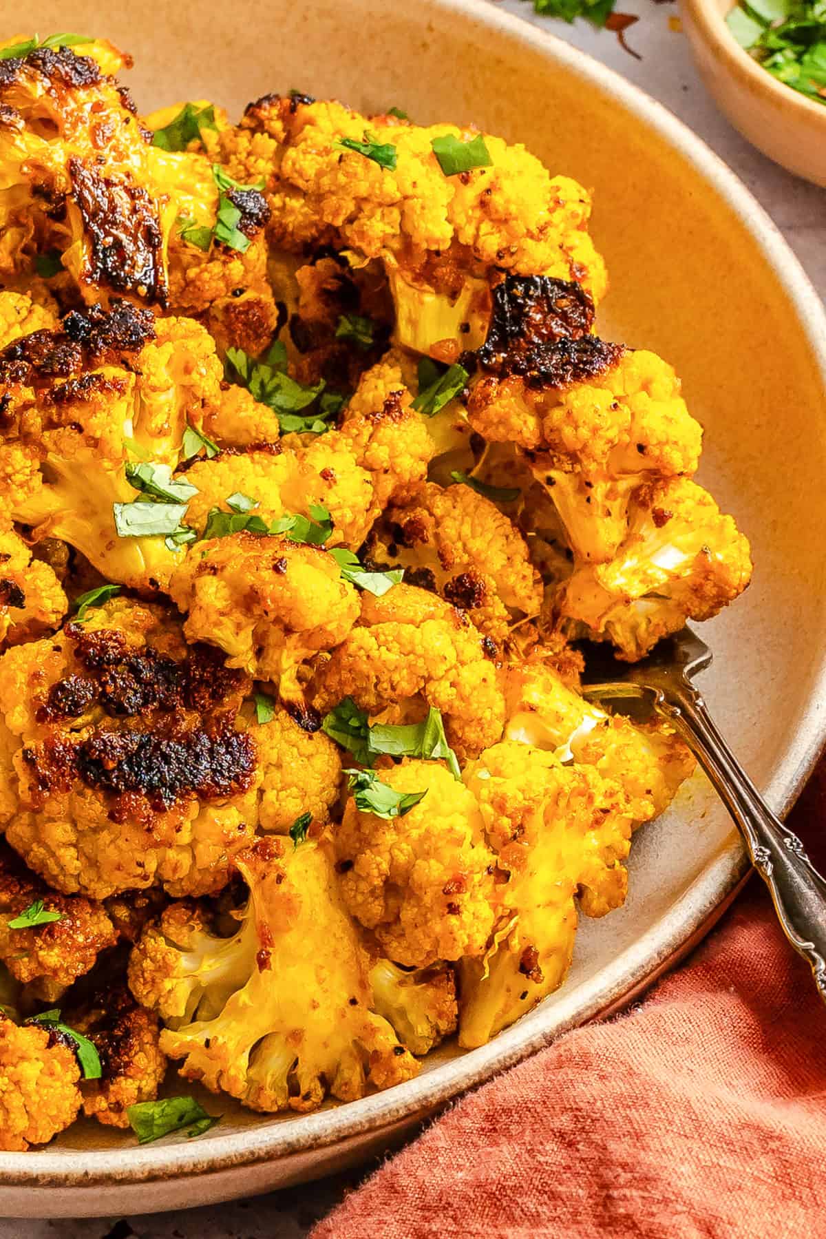Turmeric roasted cauliflower on a white serving dish garnished with fresh cilantro