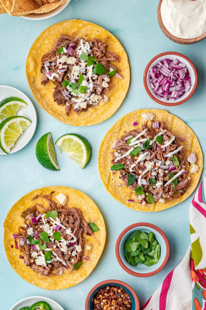 Slow Cooker Pulled Pork Tacos tacos assembled on a blue background 