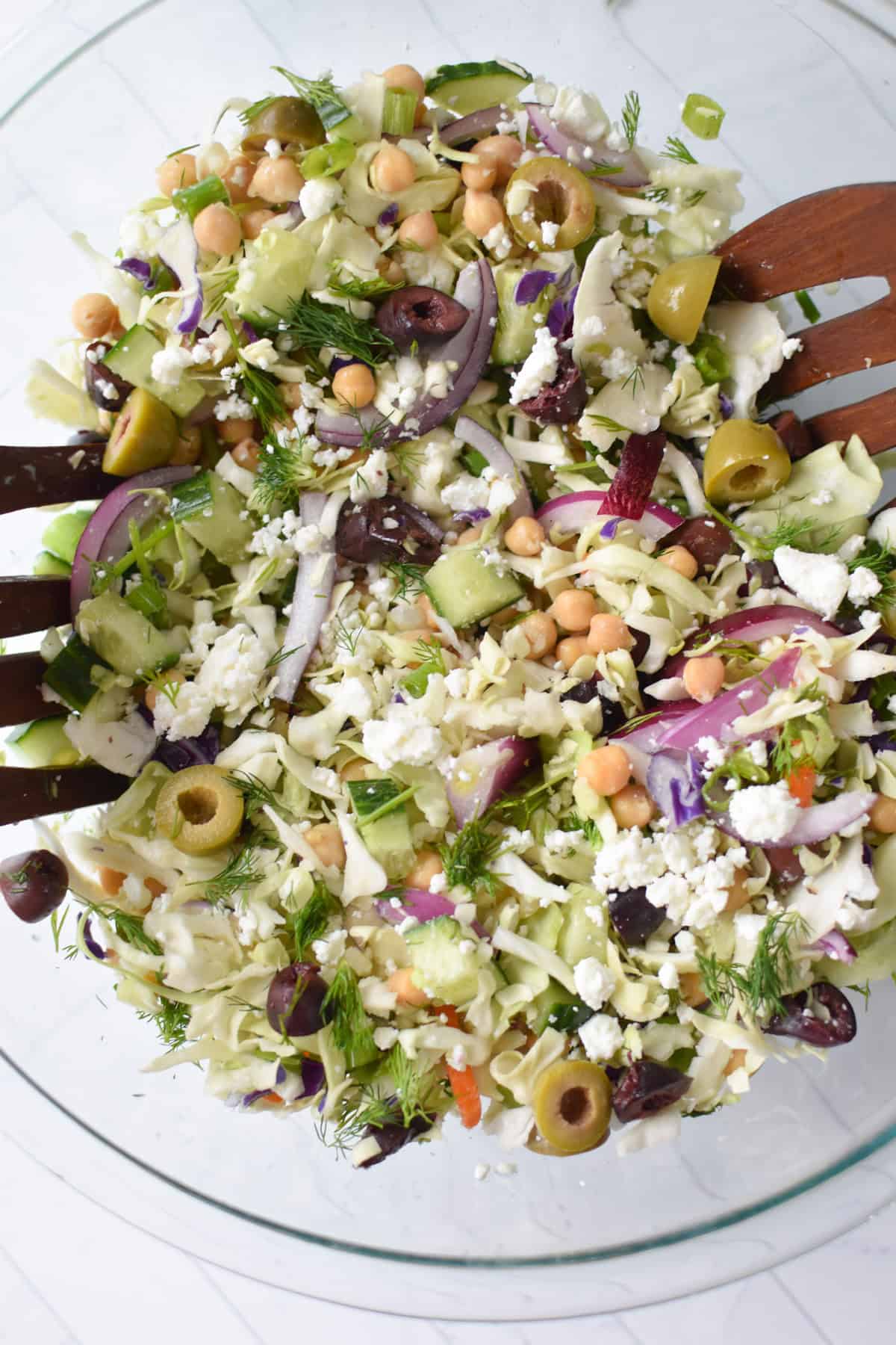 Greek Cabbage Salad in a clear glass bowl with serving spoons 