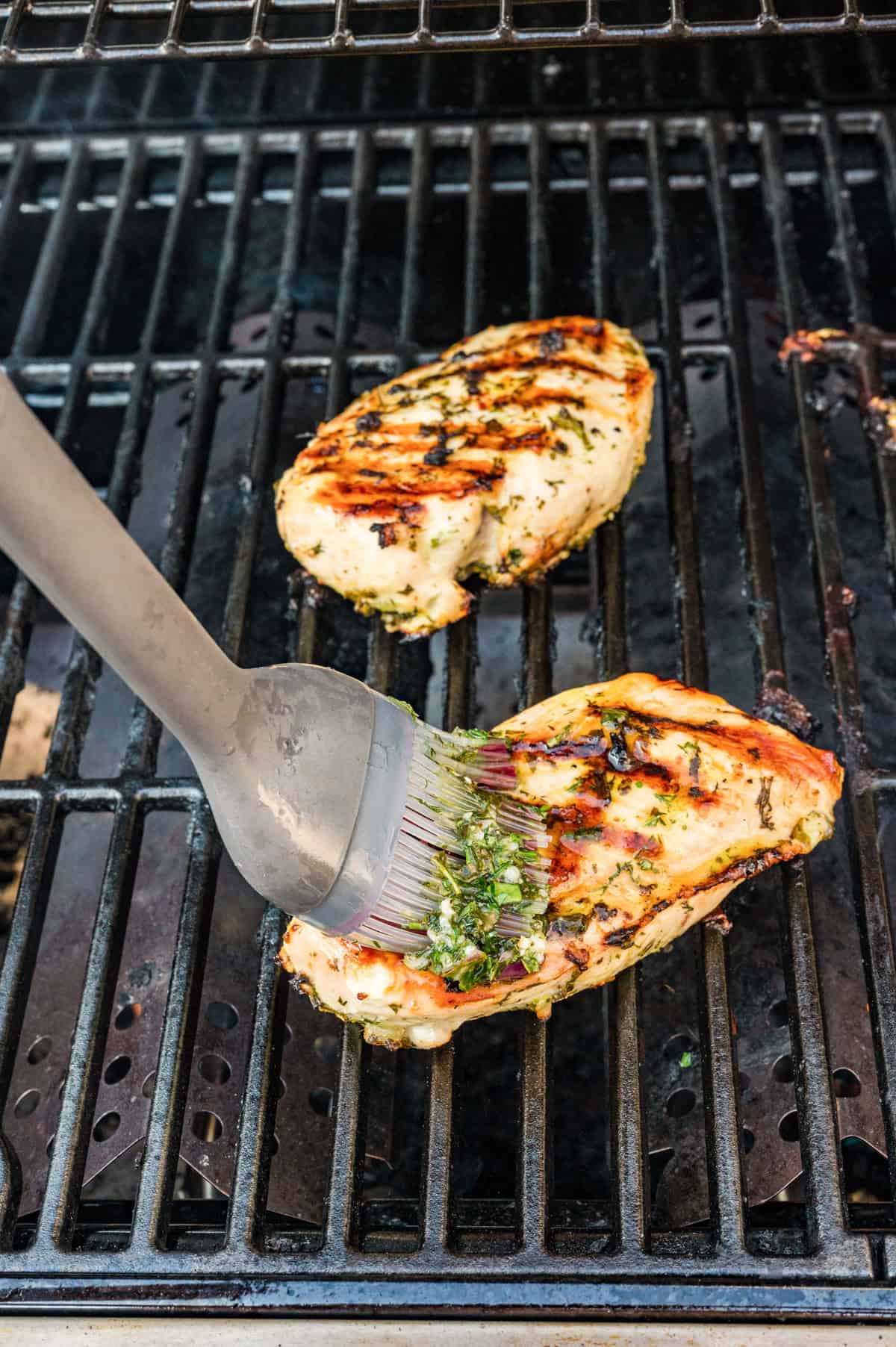 Marinated Mediterranean chicken breasts grilling with golden char marks on outdoor grill grates