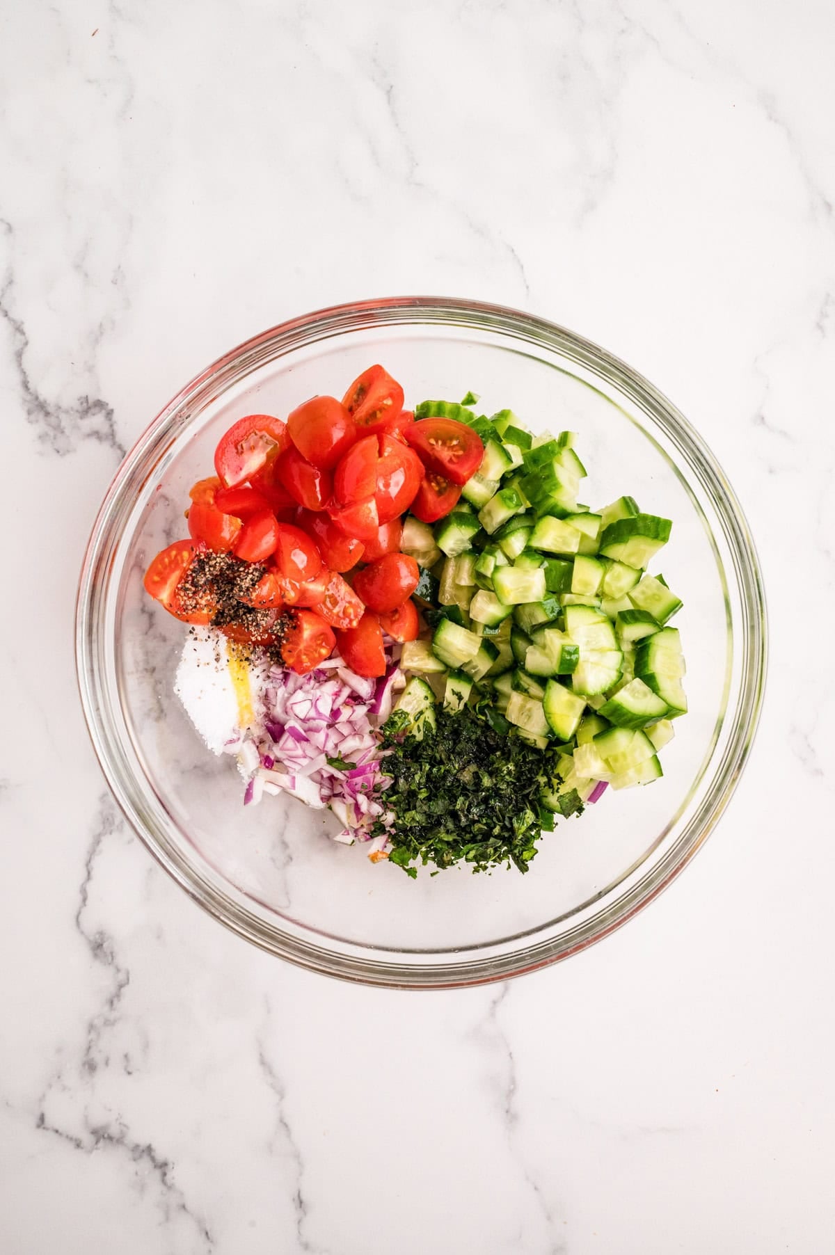 Mediterranean chicken topping with cucumber tomatoes olives and fresh basil in a mixing bowl
