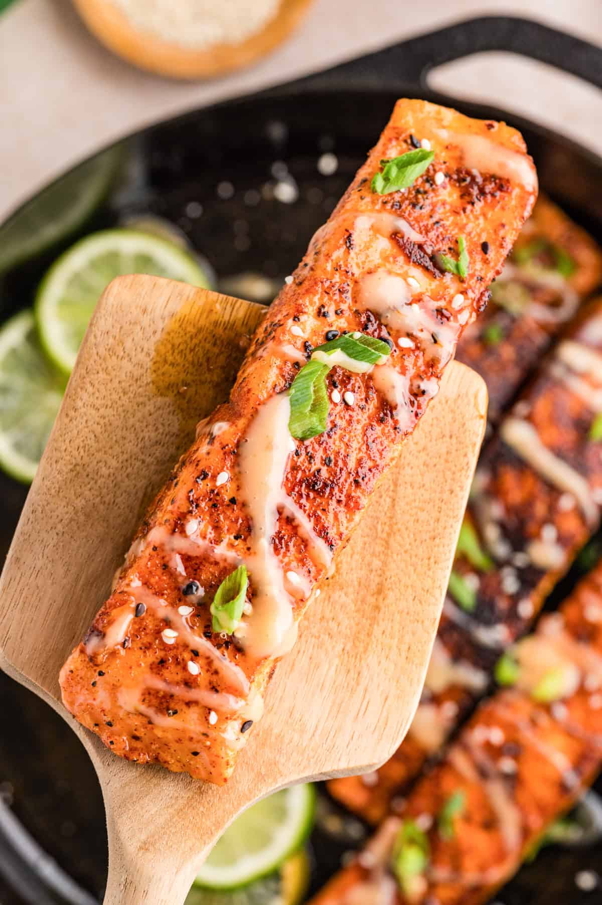 Bang bang salmon with sauce being drizzled over golden seared fillets on a spatula