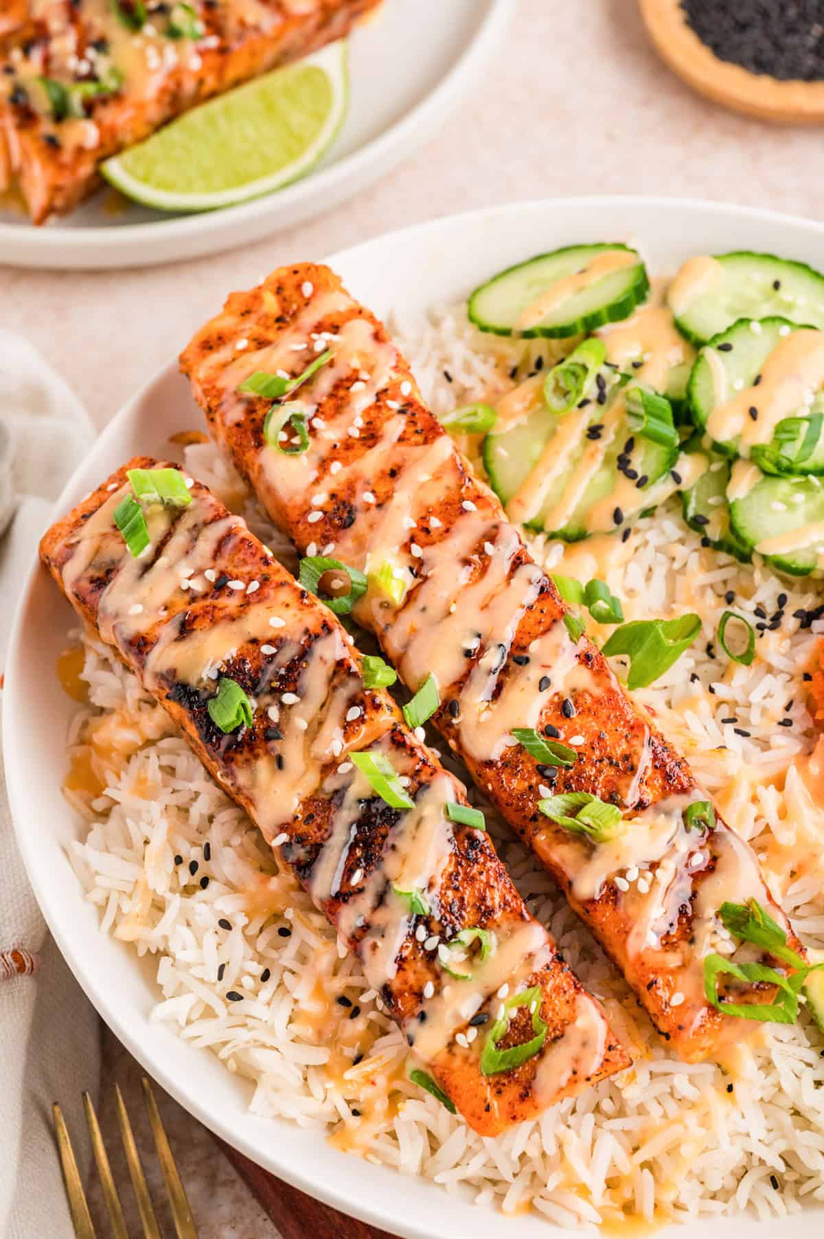 Bang bang salmon fillets topped with creamy sweet chili sauce served over rice with sliced cucumber and sesame seeds