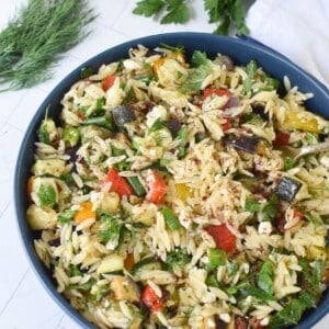 Roasted vegetable orzo salad being served from a blue bowl