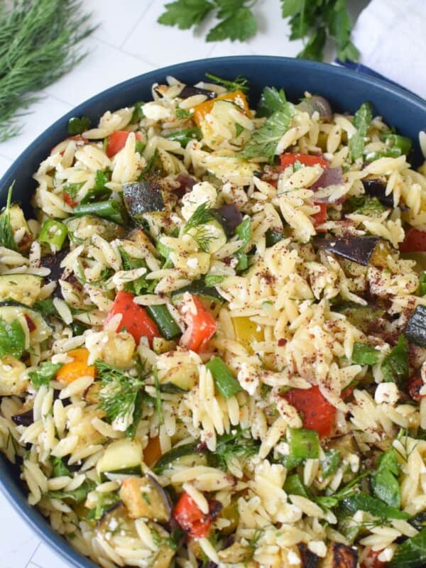 Roasted vegetable orzo salad being served from a blue bowl