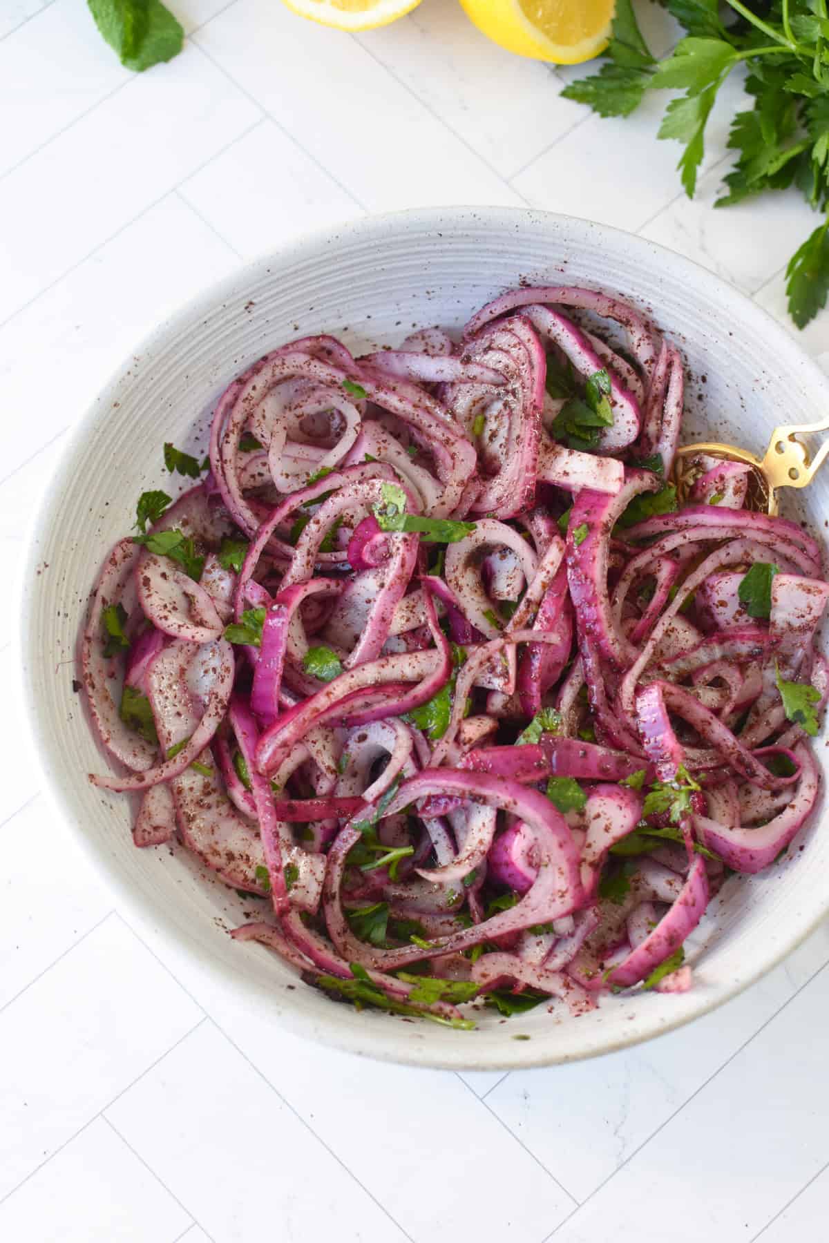 Overhead view of sumac onions in a small white bowl showing deep reddish purple color and fresh parsley