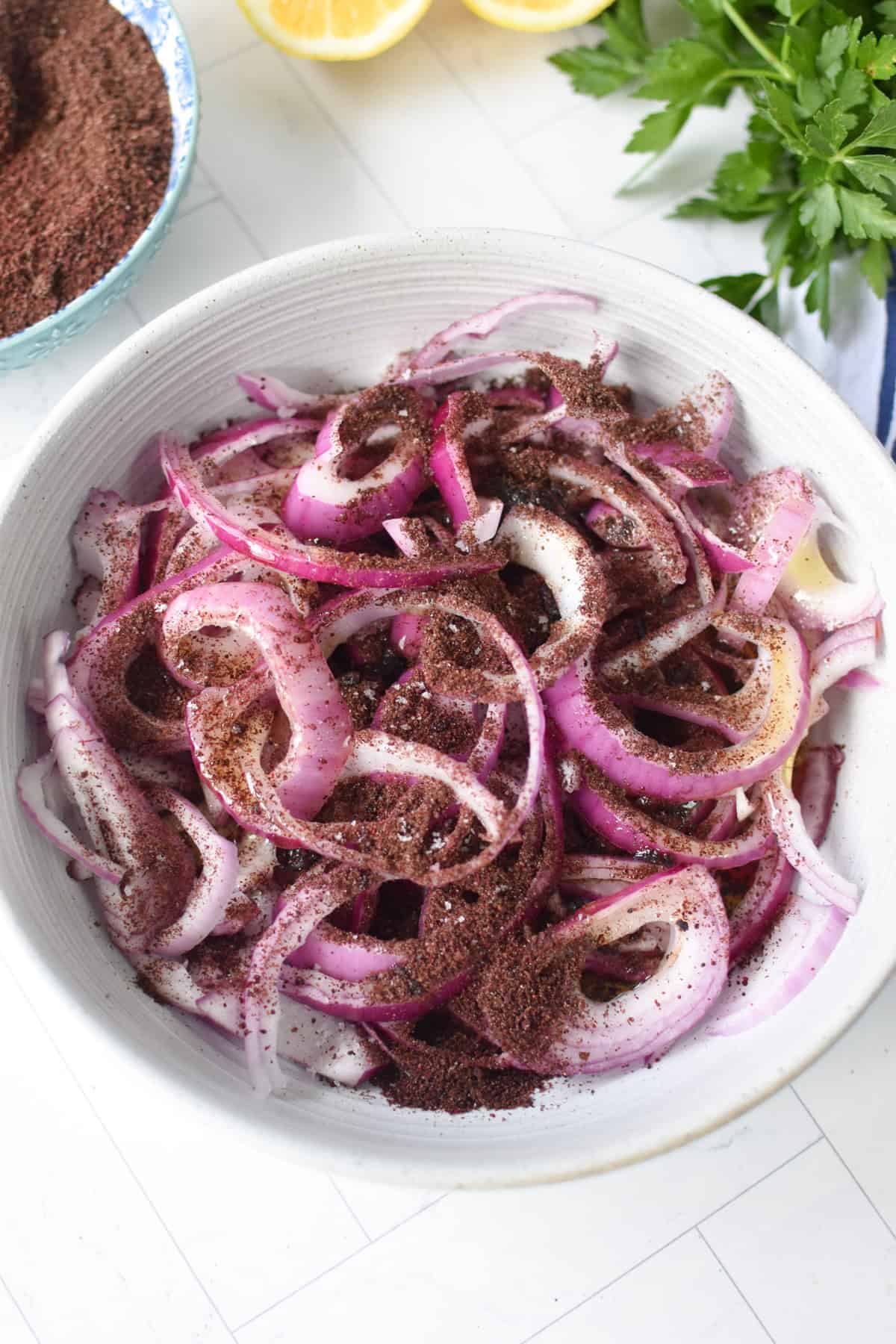 Sliced red onions in a bowl with sumac, lemon juice, red wine vinegar