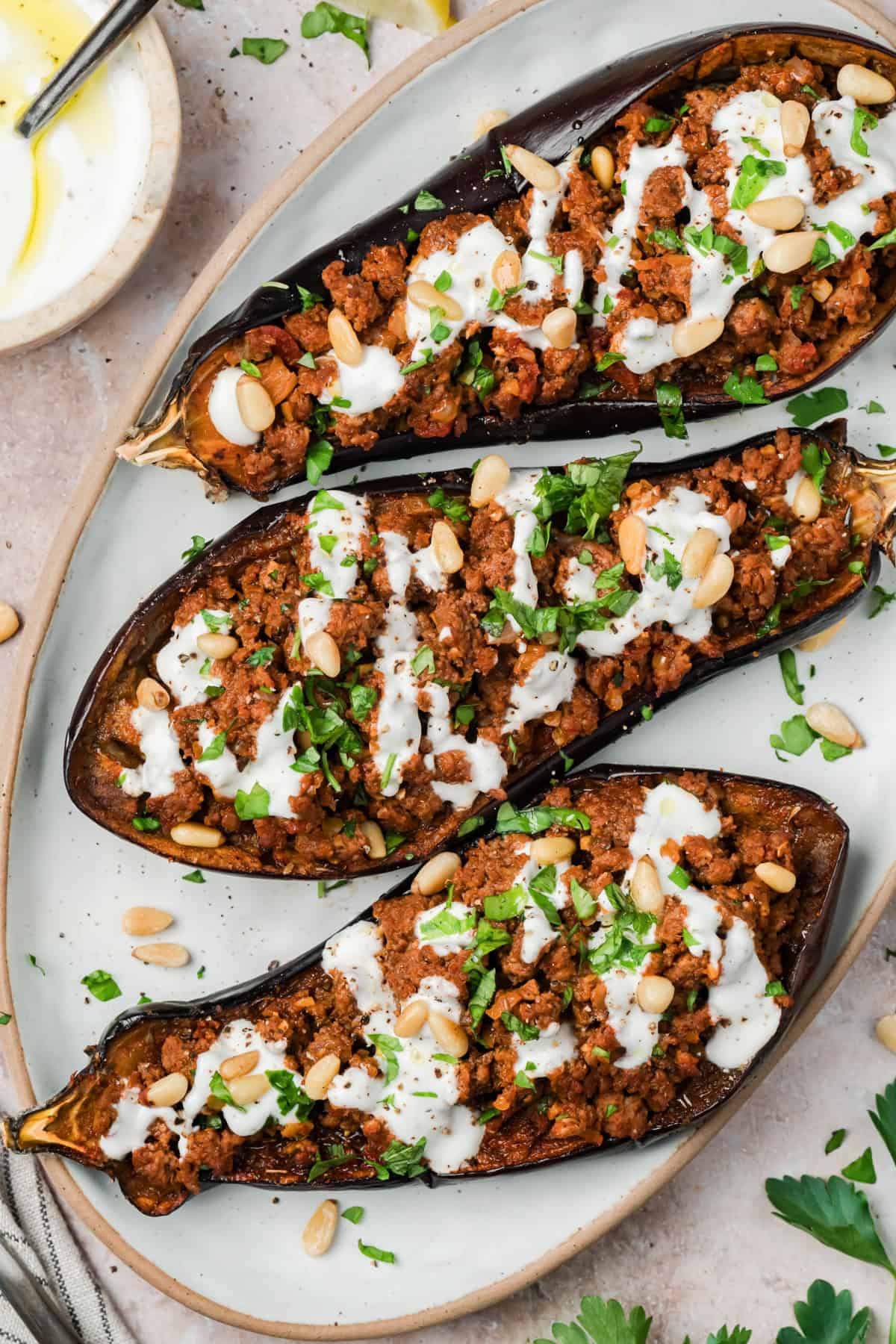 Mediterranean stuffed eggplant with ground beef and garlic yogurt sauce on a white serving dish