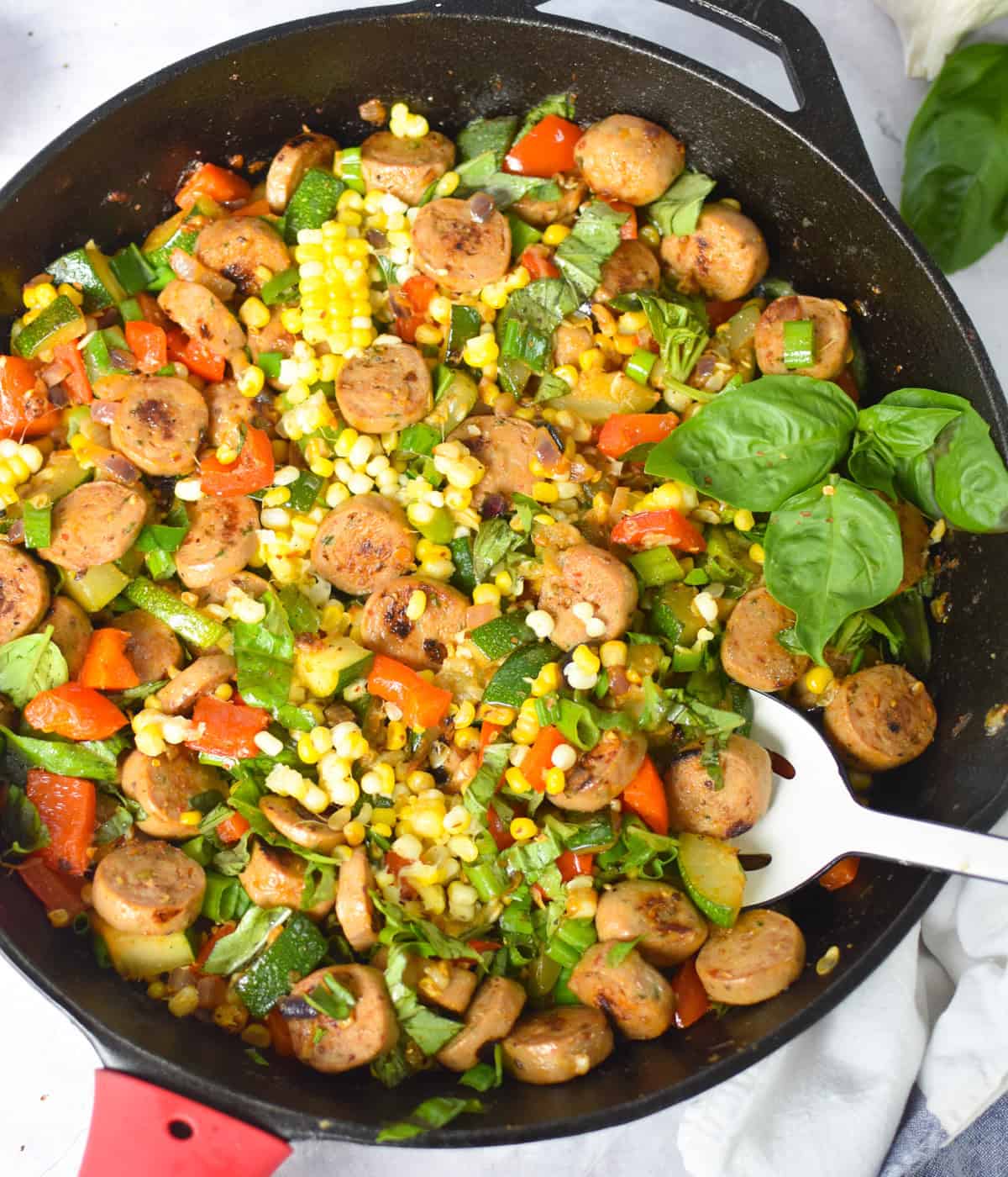 Overhead shot of one-pan sausage and veggie skillet with fresh basil on top