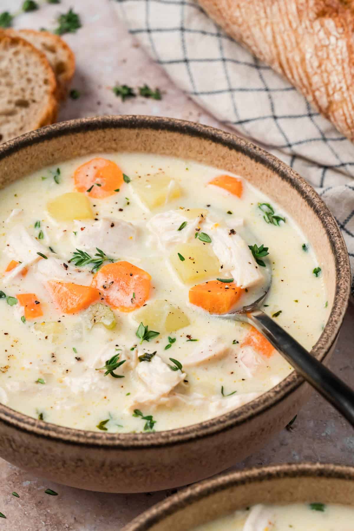 Bowl of creamy chicken potato soup topped with fresh thyme and cracked black pepper